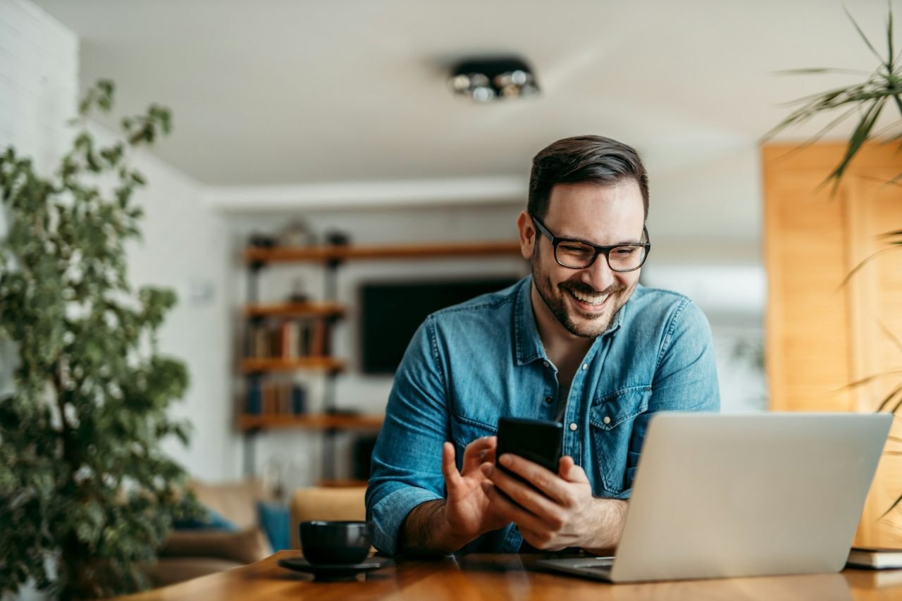 portrait of a happy man with smart phone and laptop indoors 1 1